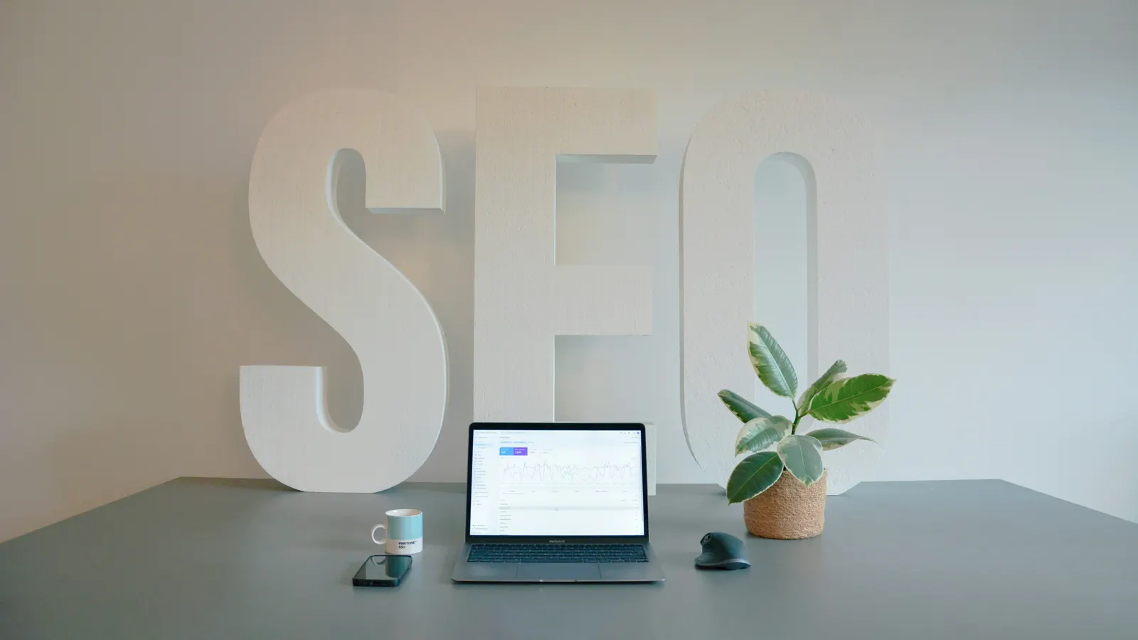 Large SEO letters beside a laptop on a desk